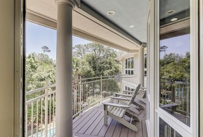 Une terrasse extérieure couverte, dotée d’une rambarde, d’une chaise en bois et offrant une vue sur des arbres et un bâtiment.