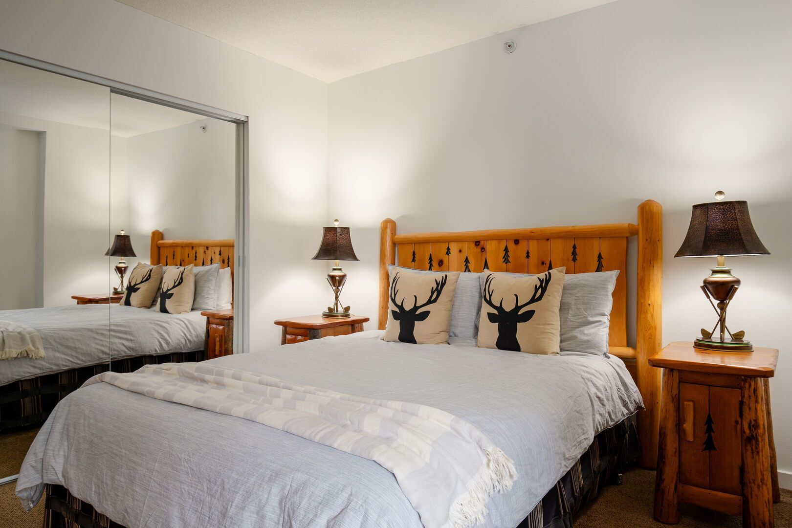 Una cama doble con cabecera de madera, dos mesitas de noche con lámparas y un espejo en la pared.