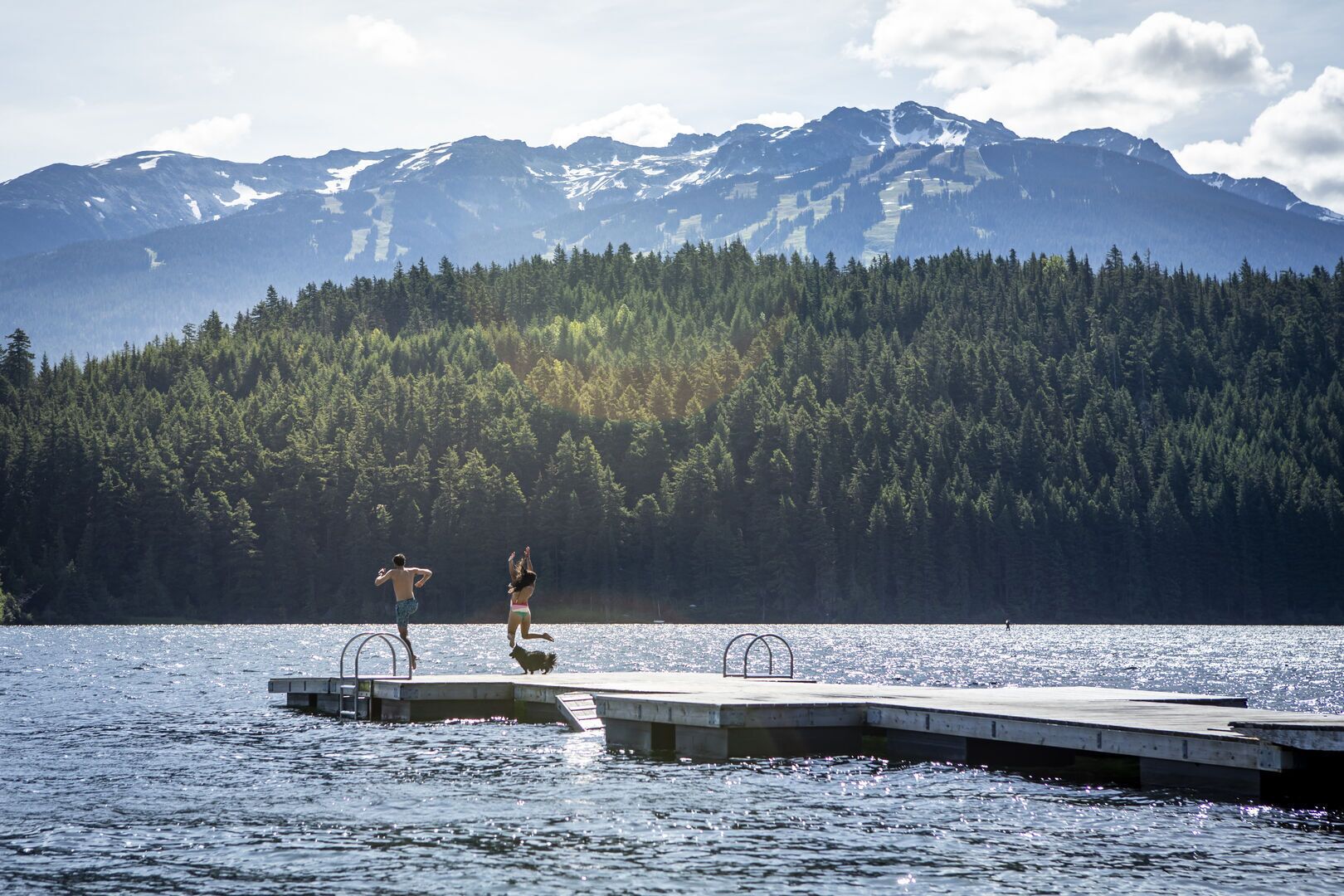 Un muelle se adentra en un lago, con una cadena montañosa boscosa al fondo.