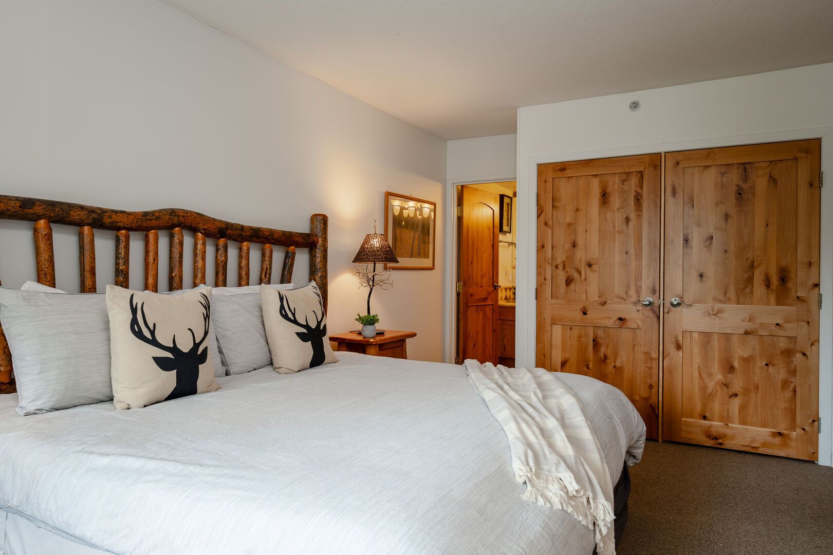 A bedroom with a large bed, a wooden headboard, a nightstand with a lamp, and a wardrobe.