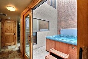Uma área de spa com hidromassagem, bancos de madeira e uma porta de vidro deslizante para um pátio.