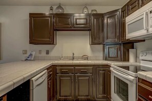 Une cuisine avec des meubles de rangement en bois foncé, un plan de travail blanc, un lave-vaisselle, une cuisinière et un four à micro-ondes.