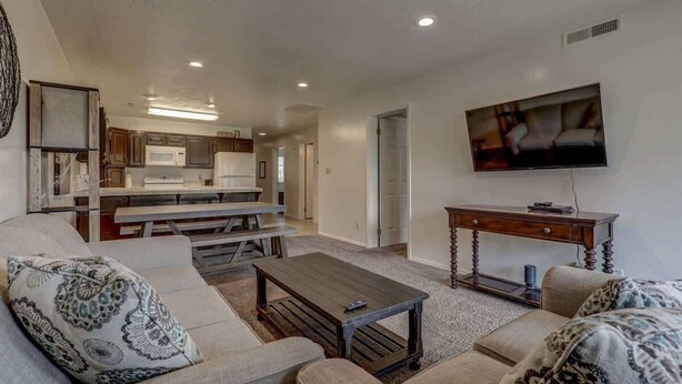 A living room with a sofa set, a coffee table, a television, and a kitchen area in the background. - Las Palmas Resort #1406 | All-Inclusive Amenities (Saint George)
