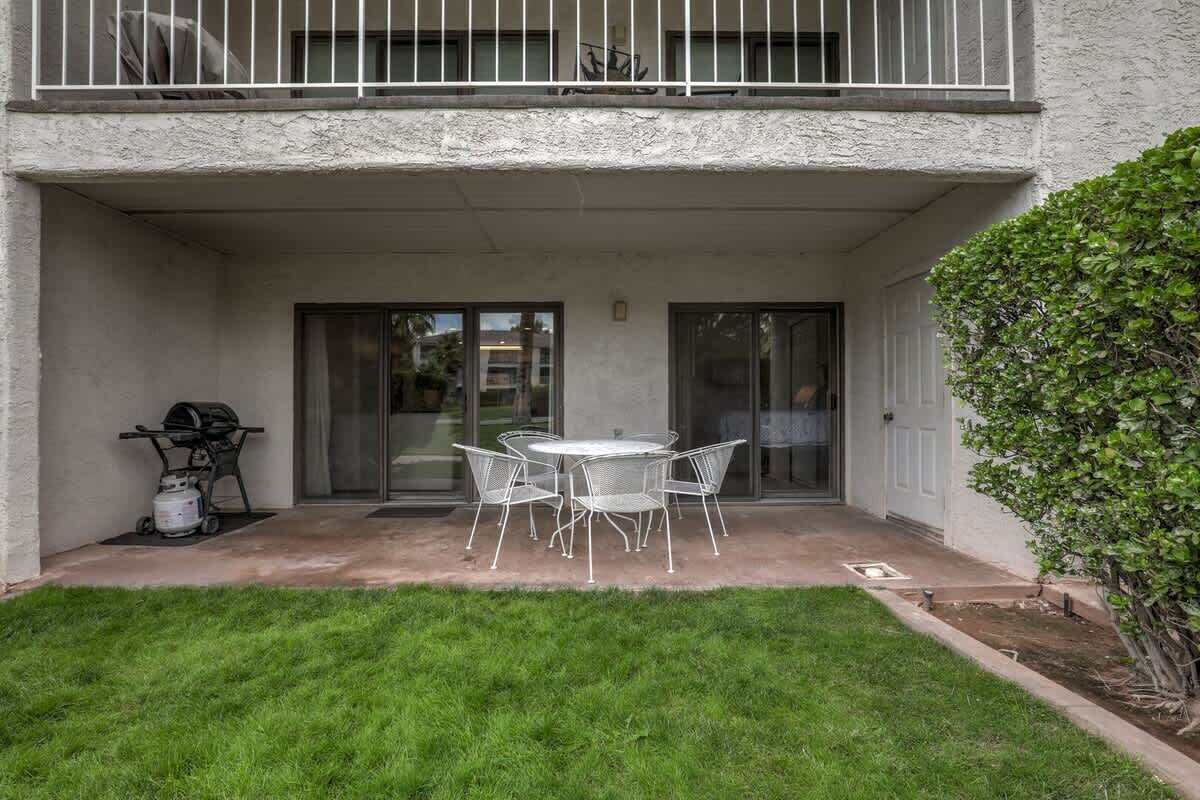 A covered patio with a table and chairs, a grill, and a small garden area.