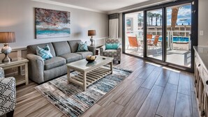 A living room with a grey sofa, a coffee table, and a patterned rug. There is a painting on the wall and a window with a view of a pool and palm trees. - WALK OUT TO POOL FROM FURNISHED PATIO!  Beachside Condo, Just Steps to Beach! (Miramar Beach)