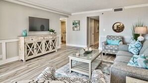 A living room with a wooden floor, a sofa, a coffee table, and a TV on a wooden cabinet. - WALK OUT TO POOL FROM FURNISHED PATIO!  Beachside Condo, Just Steps to Beach! (Miramar Beach)