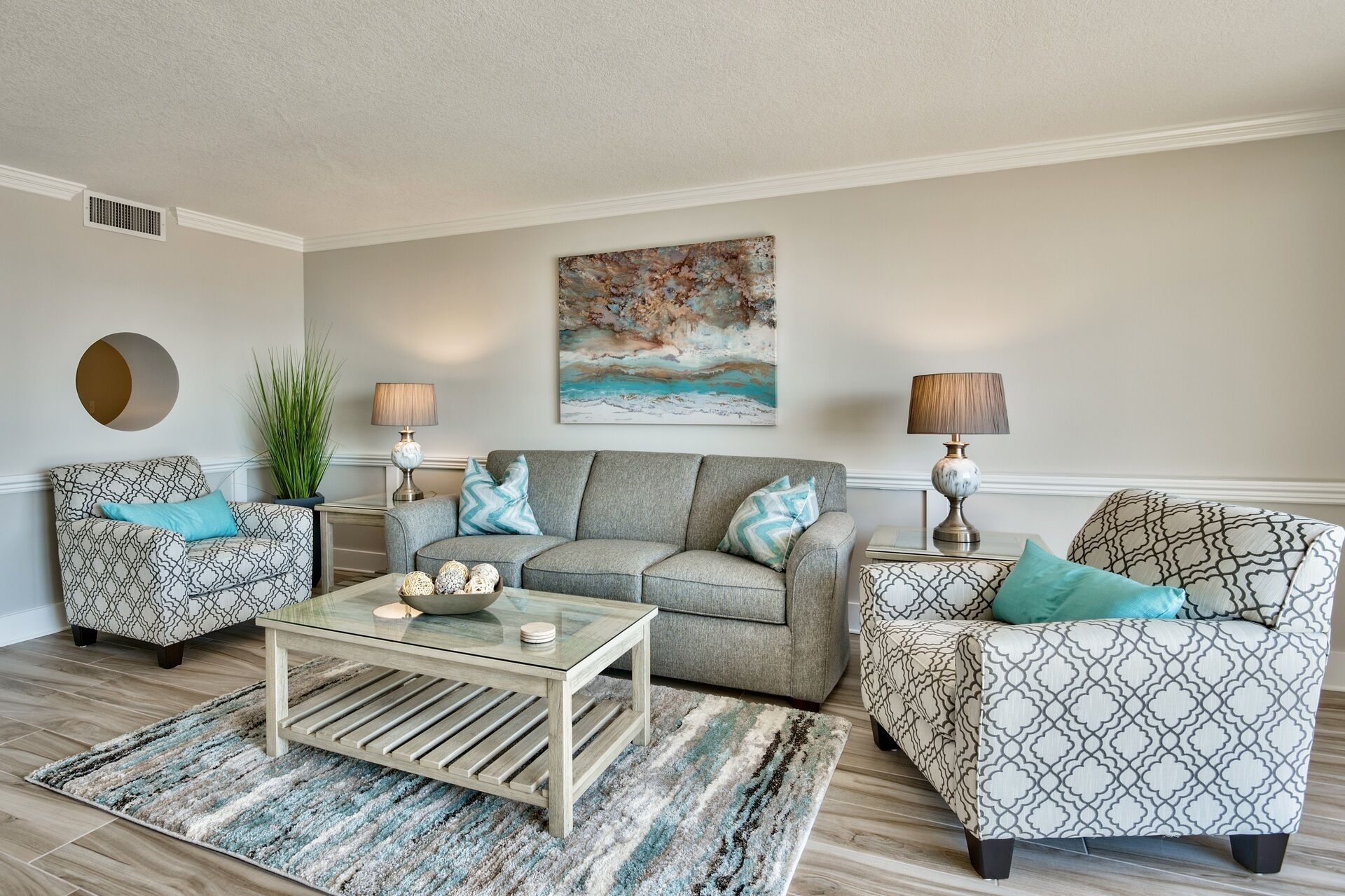 A living room with a grey sofa, patterned armchairs, a coffee table, and a painting on the wall.