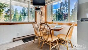 A dining area with a table, chairs, a television mounted on the wall, and a view of trees through large windows. - Sunny, Corner Unit. Private Kitchenette. Ski In - Walk to Town | PM4D (Breckenridge)