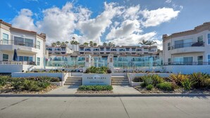 A modern hotel with a central glass facade, multiple balconies, and a sign reading 'SAN MIGUEL 500 NORTH - THE STRAND'. - Premium Beachfront Stay Ground Floor, 2 Parking Spots,  Community Jacuzzi EV Charging (Oceanside)