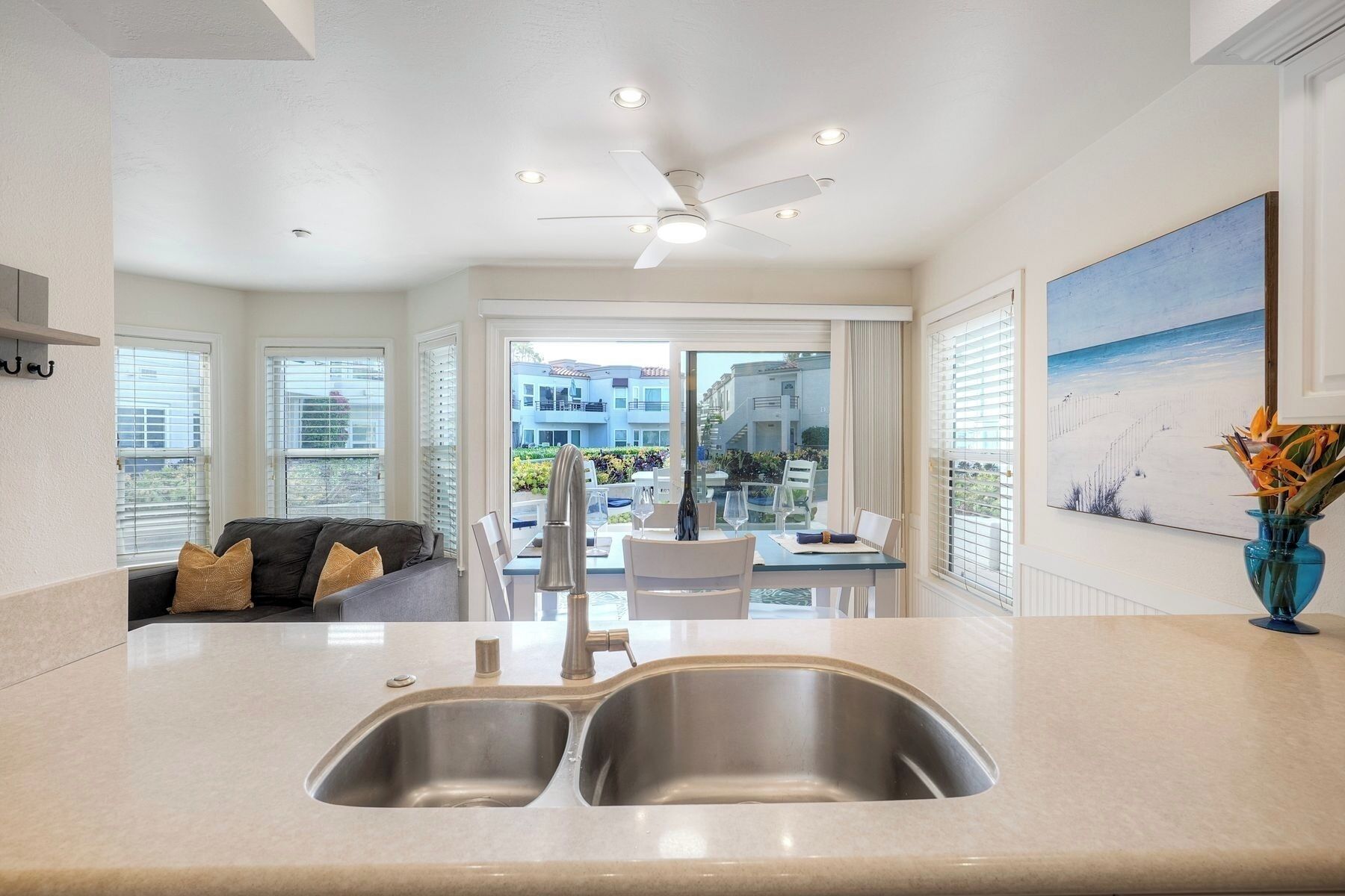 A modern kitchen with a double sink, a ceiling fan, and a dining area with a view of the cityscape.