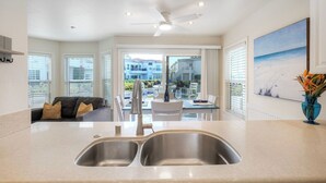 A modern kitchen with a double sink, a ceiling fan, and a dining area with a view of the cityscape. - Premium Beachfront Stay Ground Floor, 2 Parking Spots,  Community Jacuzzi EV Charging (Oceanside)