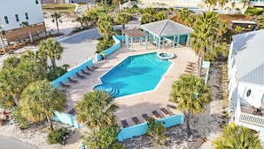 An aerial view of a resort with a swimming pool, lounge chairs, and palm trees.