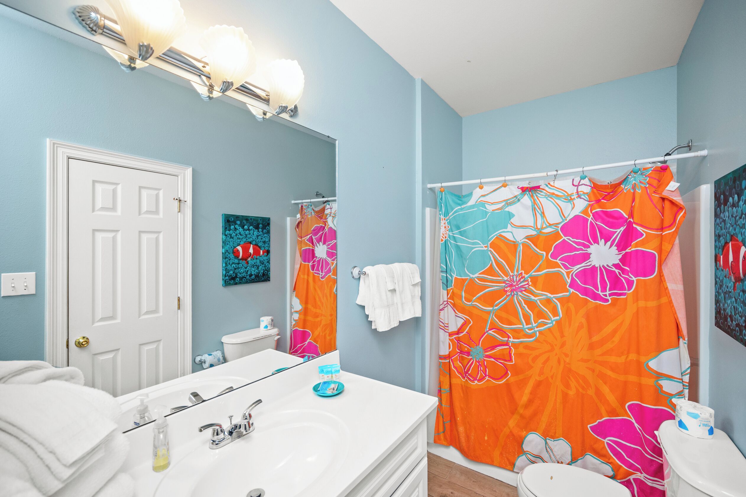 A bathroom with a white vanity, a large mirror, a shower curtain with floral patterns, and a light blue wall.