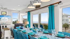 Un comedor con una mesa dispuesta para seis, ventanas amplias y vista al océano.