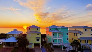 Una hilera de casas de playa coloridas con un atardecer de fondo.