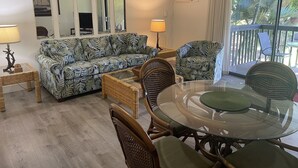 A living room with a sofa, chairs, a glass table, and a lamp. There are mirrors on the wall and an air conditioning unit.