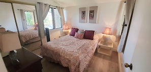Ein Schlafzimmer mit einem großen Bett, zwei Nachttischen mit Lampen, einem Spiegel und zwei gerahmten Bildern an der Wand.