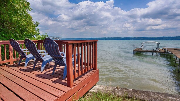 A wooden deck with Adirondack chairs overlooking a lake.
