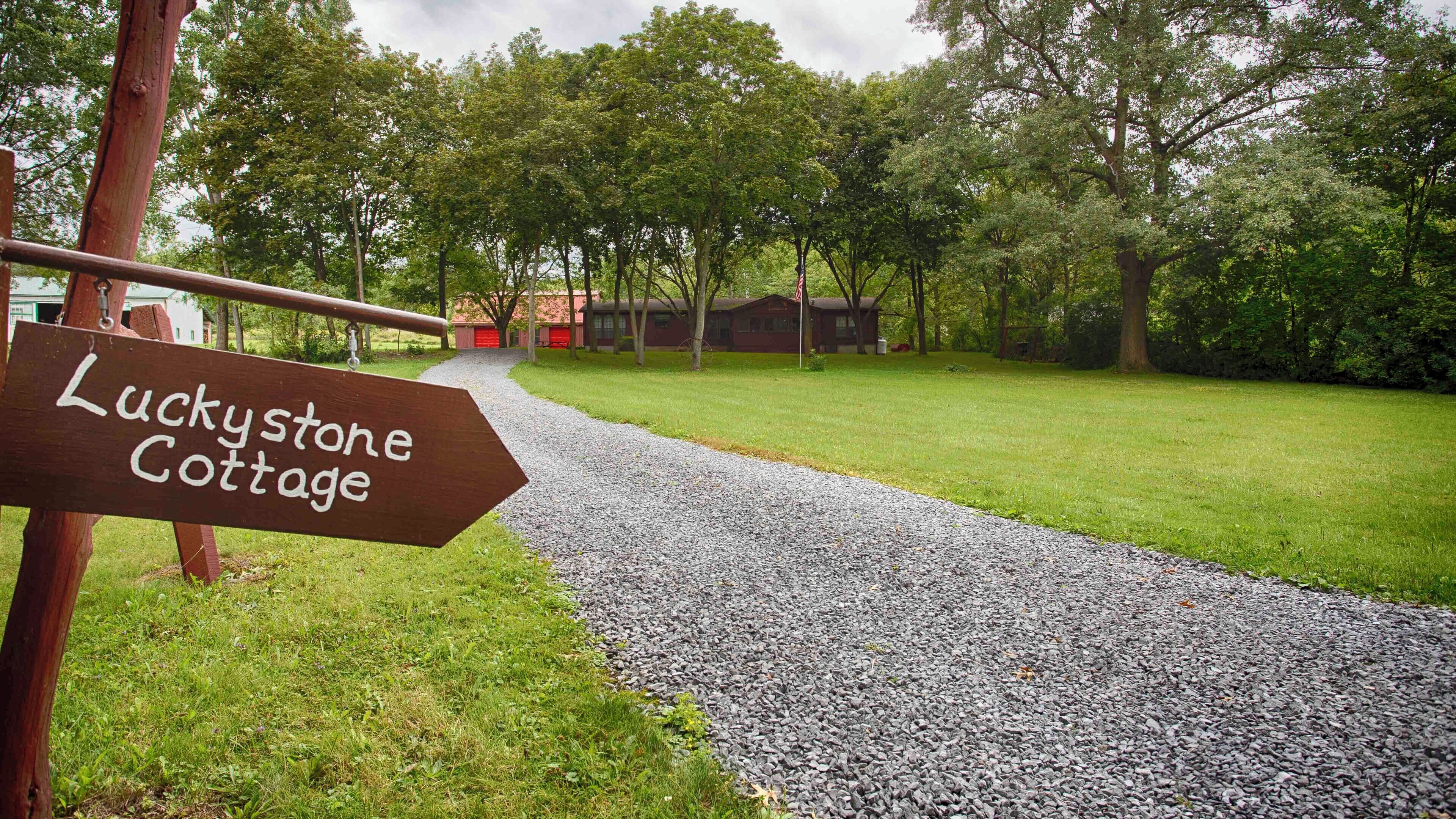 Un sendero de grava que conduce a una construcción rústica con la leyenda 'Luckystone Cottage'.