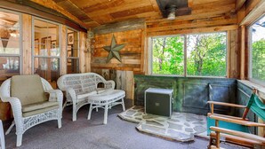A cozy cabin interior with wicker furniture, a star decoration, a stone fireplace, and a view of greenery outside.