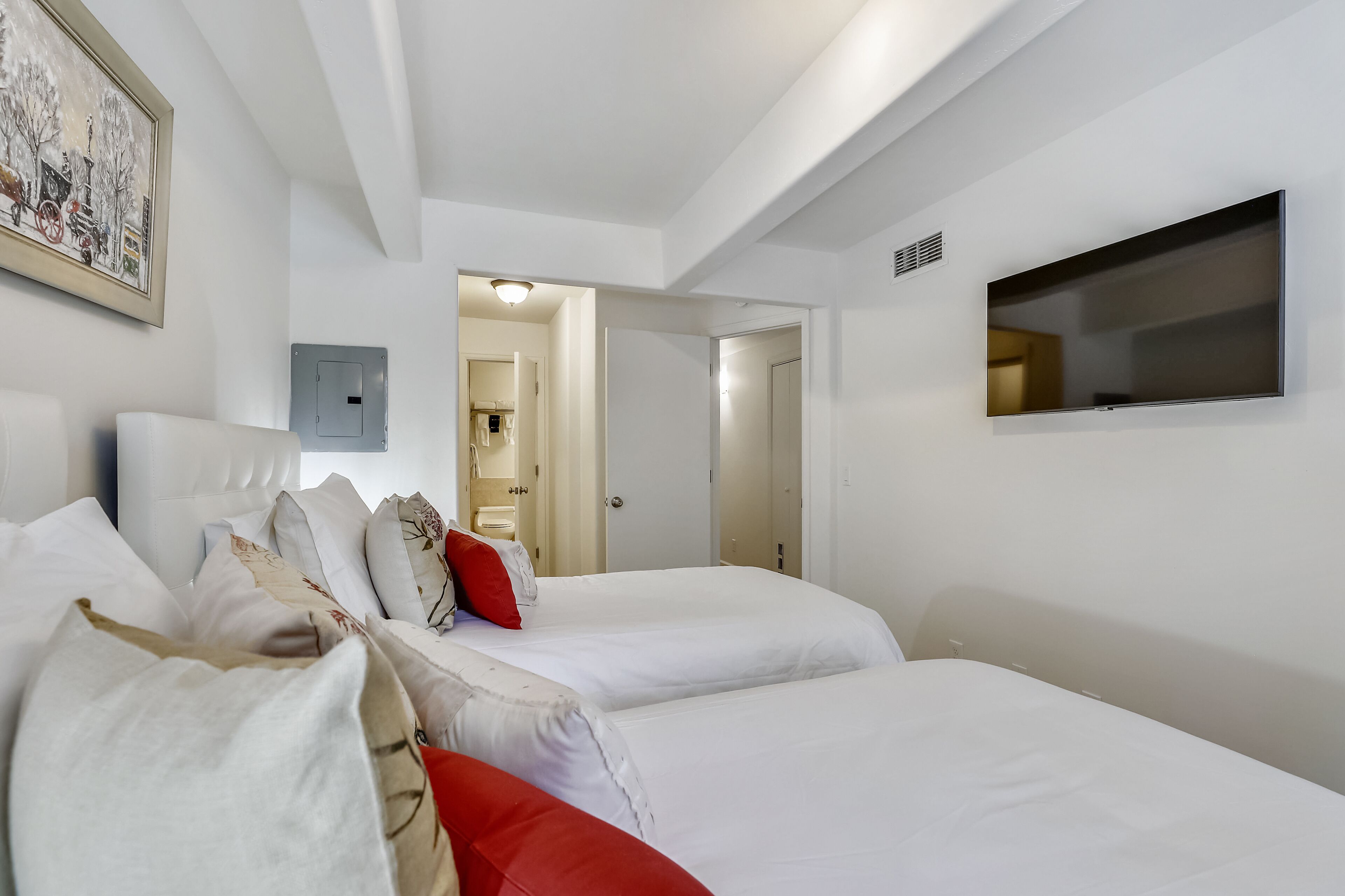A hotel room with two beds, a flat-screen TV, and a painting on the wall.