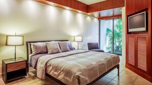 Een moderne slaapkamer met een groot bed, twee nachtkastjes met lampen, een televisie bevestigd aan een houten kast, en uitzicht op groen door een groot raam.