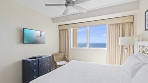 Quarto de hotel com cama, televisão na parede, ventoinha no teto e janela com cortinas.