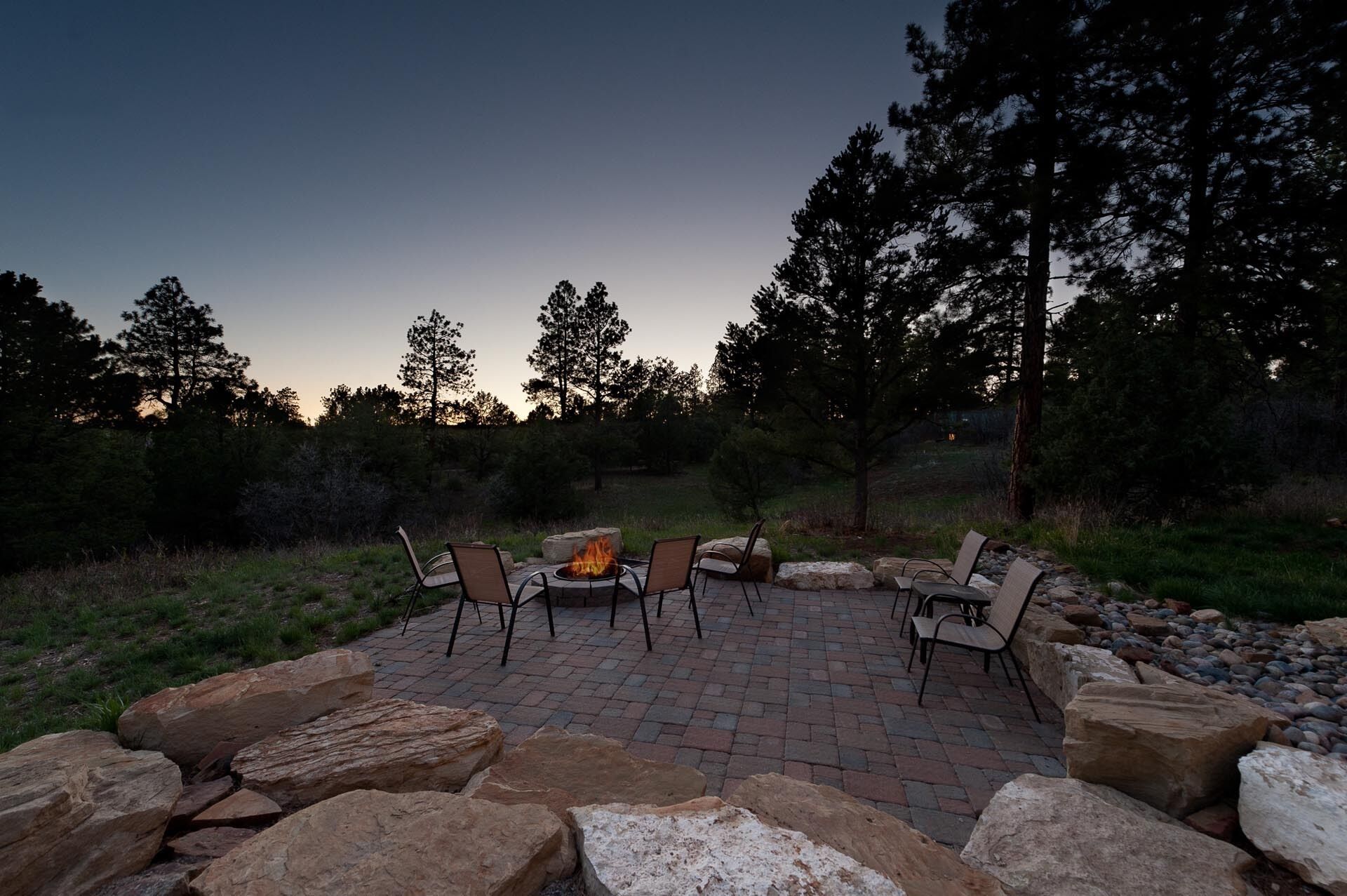An outdoor patio with a fire pit and seating area surrounded by rocks and trees.