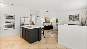 A modern kitchen with a central island, built-in oven, and a dining area with a bench. - EV_116 - 6BR / 4.5BA Highlands Reserve Villa near Disney, Private Pool & Spa (Davenport)