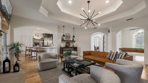 Amplio salón con un sofá moderno, sillones y una mesa de centro. Se observa una cocina al fondo con una isla grande y una zona de comedor.