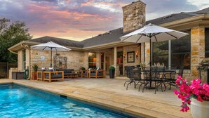 Zona junto a la piscina con muros de piedra, mobiliario exterior y una parrilla.