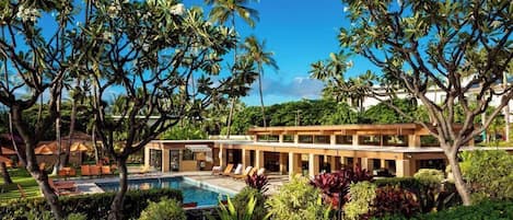 A resort with a swimming pool, palm trees, and a modern building with lounge chairs.