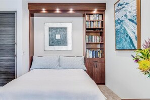 A bedroom with a bed, a bookshelf, a painting, and a door.