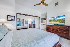 A bedroom with a bed, a TV, a ceiling fan, and a dresser.
