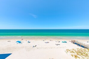 A beach with white sand, clear turquoise water, and a pier with people.