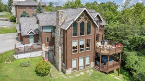 Une cabane en rondins à deux étages, dotée d’une cheminée en pierre, d’un balcon avec des meubles d’extérieur et d’une grande fenêtre.