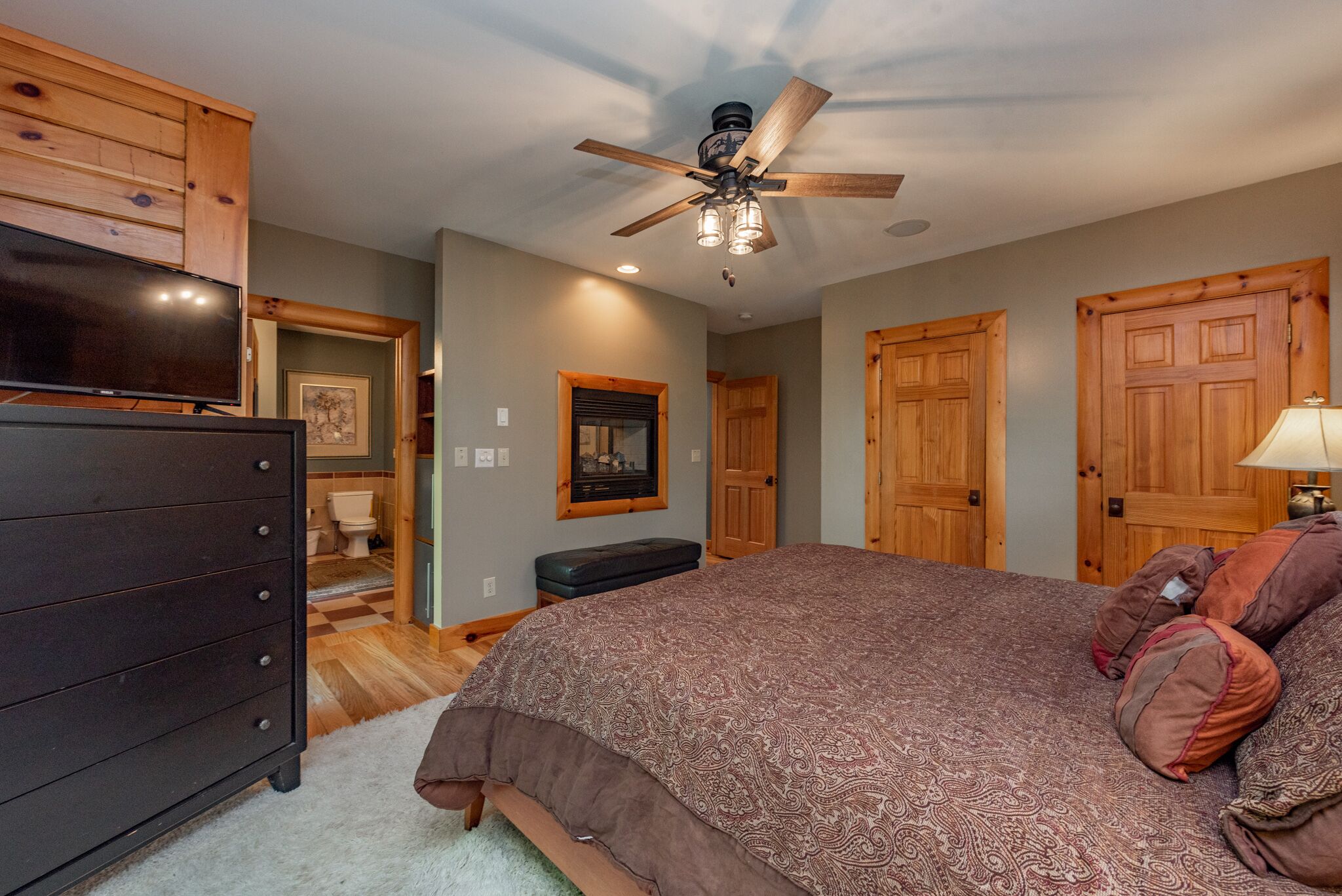 A bedroom with a large bed, wooden wardrobe, ceiling fan, and a television.