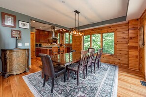 A spacious dining area with a large wooden table, surrounded by chairs, in a cabin-style interior with wooden walls and large windows. - Elegant Ski-In/Out Lodge w/ Fireplaces & Hot Tub (McHenry)