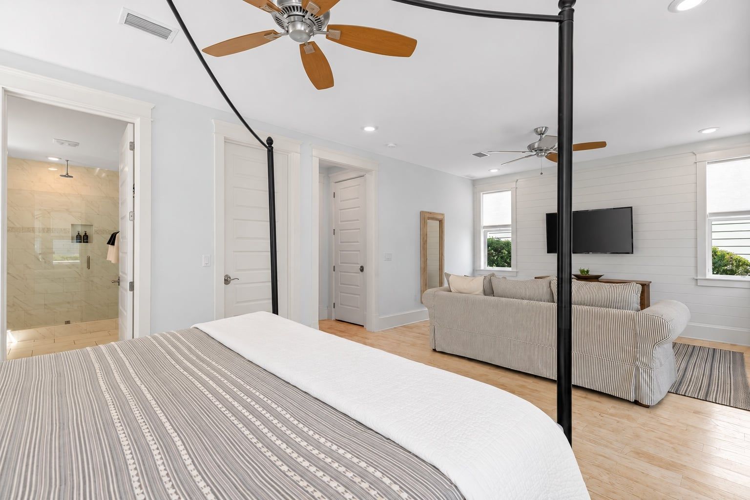 Un dormitorio moderno con una cama grande, un ventilador de techo y vistas a una sala de estar con un sofá y un televisor.