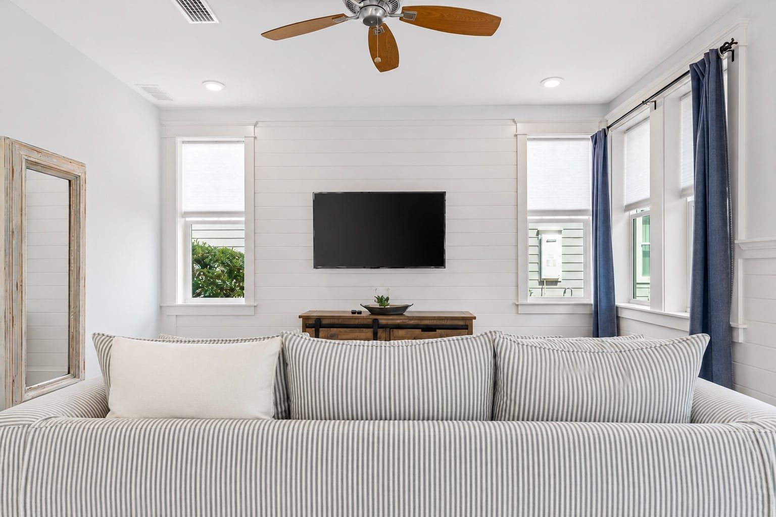 A bedroom with a bed, a TV mounted on the wall, a ceiling fan, and a window with curtains.