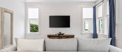 A bedroom with a bed, a TV mounted on the wall, a ceiling fan, and a window with curtains.
