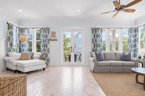 A spacious living room with two sofas, a ceiling fan, and a view through a glass door to the outside.