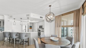 A modern kitchen with white cabinets, a central island, and bar stools. - WELL APPOINTED & ELEGANT CONDO! GULF FRONT WITH SWEEPING VIEW (Destin)