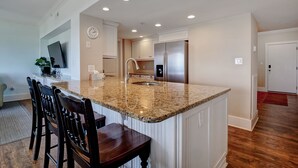 A kitchen with a granite countertop, stainless steel refrigerator, and white cabinetry. - DR 2211–Simply elegant oceanfront condo with expansive views, pool and tennis (Wrightsville Beach)