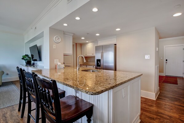A kitchen with a granite countertop, stainless steel refrigerator, and white cabinetry.