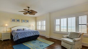 A bedroom with a bed, a chair, a ceiling fan, and a window with blinds.