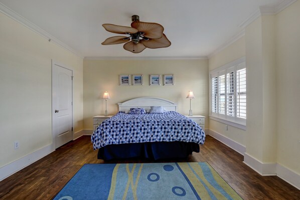A bedroom with a bed, a ceiling fan, bedside lamps, a window with blinds, and a rug.
