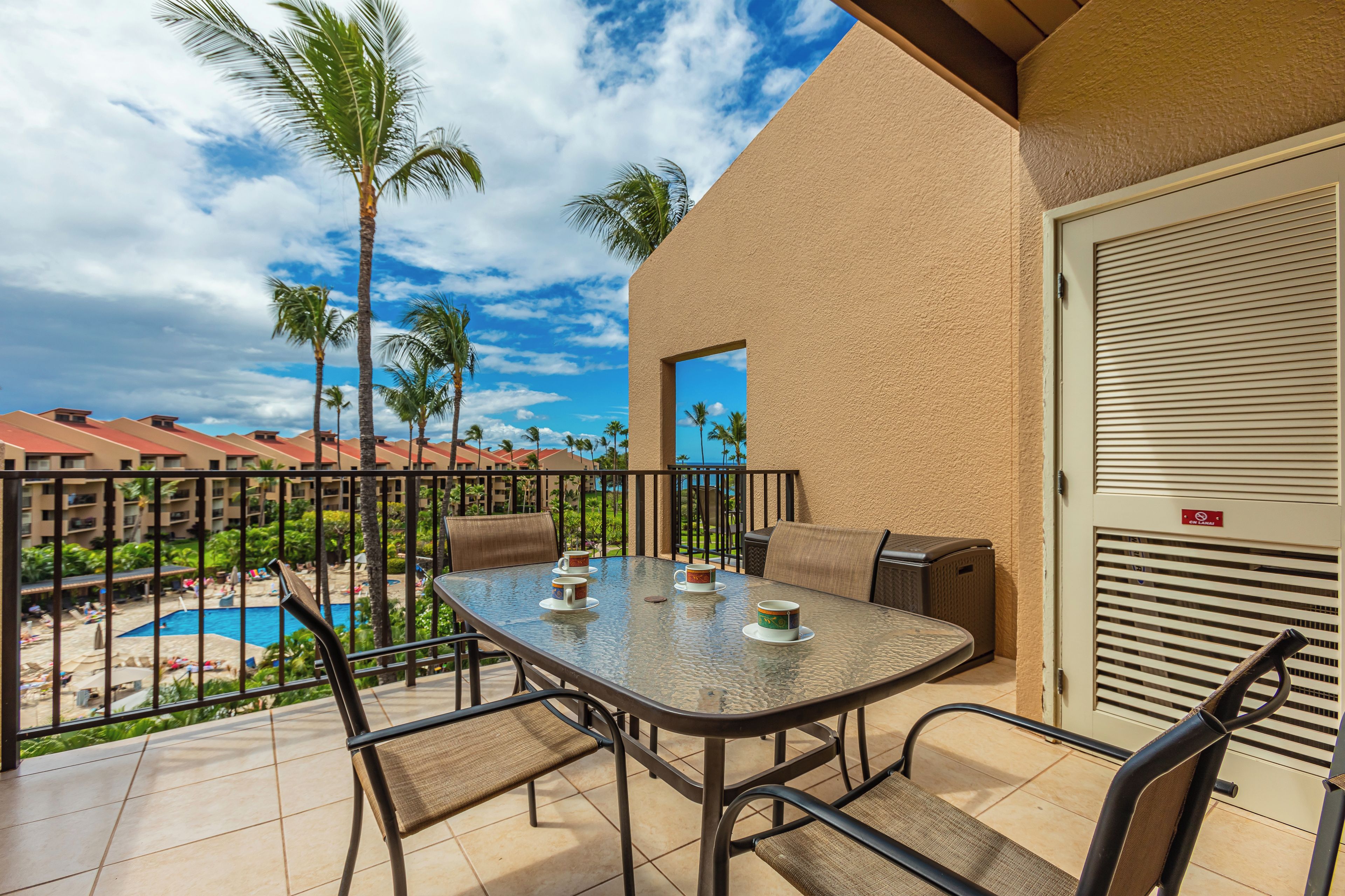 Un balcon avec une table, des chaises et une vue sur une piscine et des palmiers.