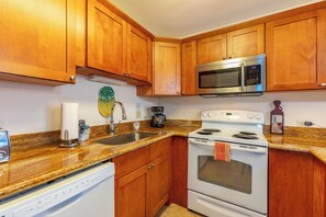 A kitchen with wooden cabinets, a stainless steel microwave, a white stove, and a granite countertop.