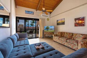 A living room with a blue sofa, a floral-patterned sofa, a TV, and a ceiling fan.